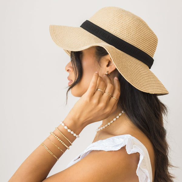 Fourth Info Card, A woman in a straw hat with a black ribbon wears delicate gold jewelry, including rings, bracelets, and a pearl necklace.