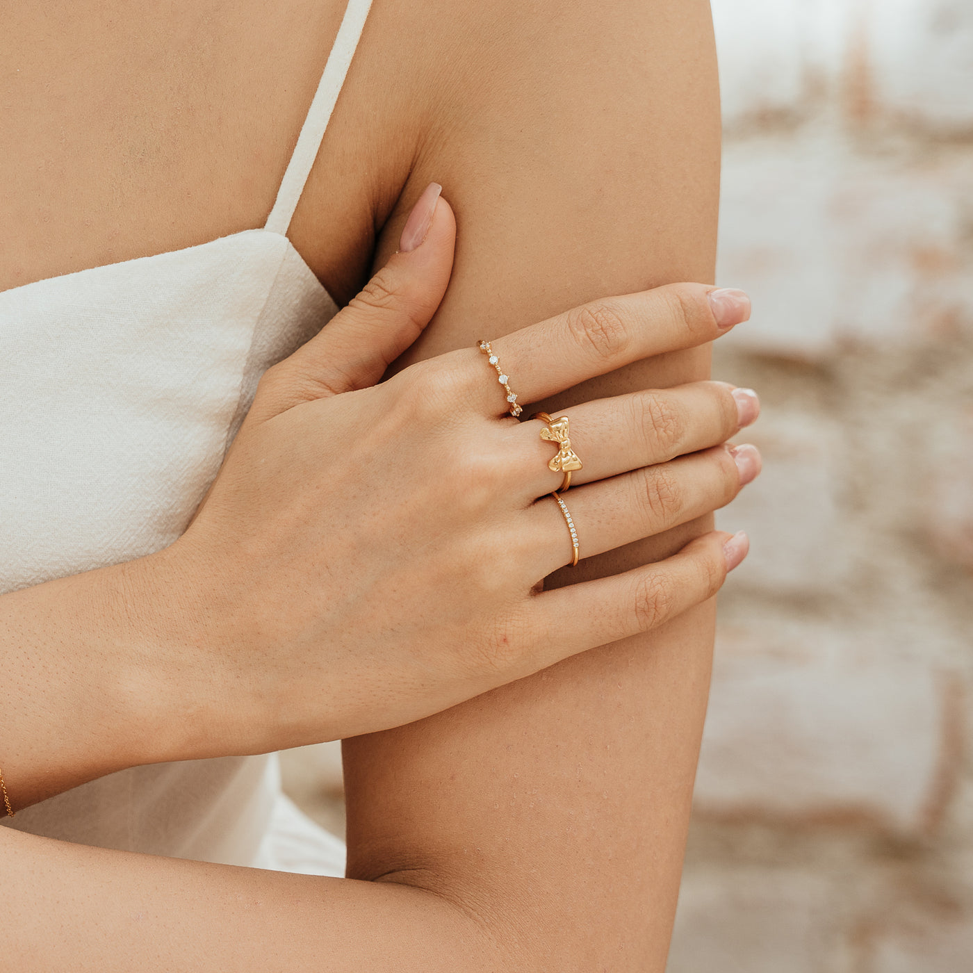 Close-up of a woman’s hand resting on her opposite arm, wearing a CZ Floating Ring, Ribbon Bow Ring, and Pavé CZ Ring.