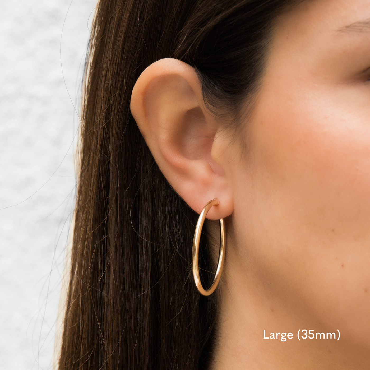 Woman wearing a single large 35mm gold Everyday Hoop Earring on one ear. The photo is taken from the side, showing her earring, and hair pulled back.

Large (35mm) Everyday Hoop Earrings by Simple & Dainty Jewelry