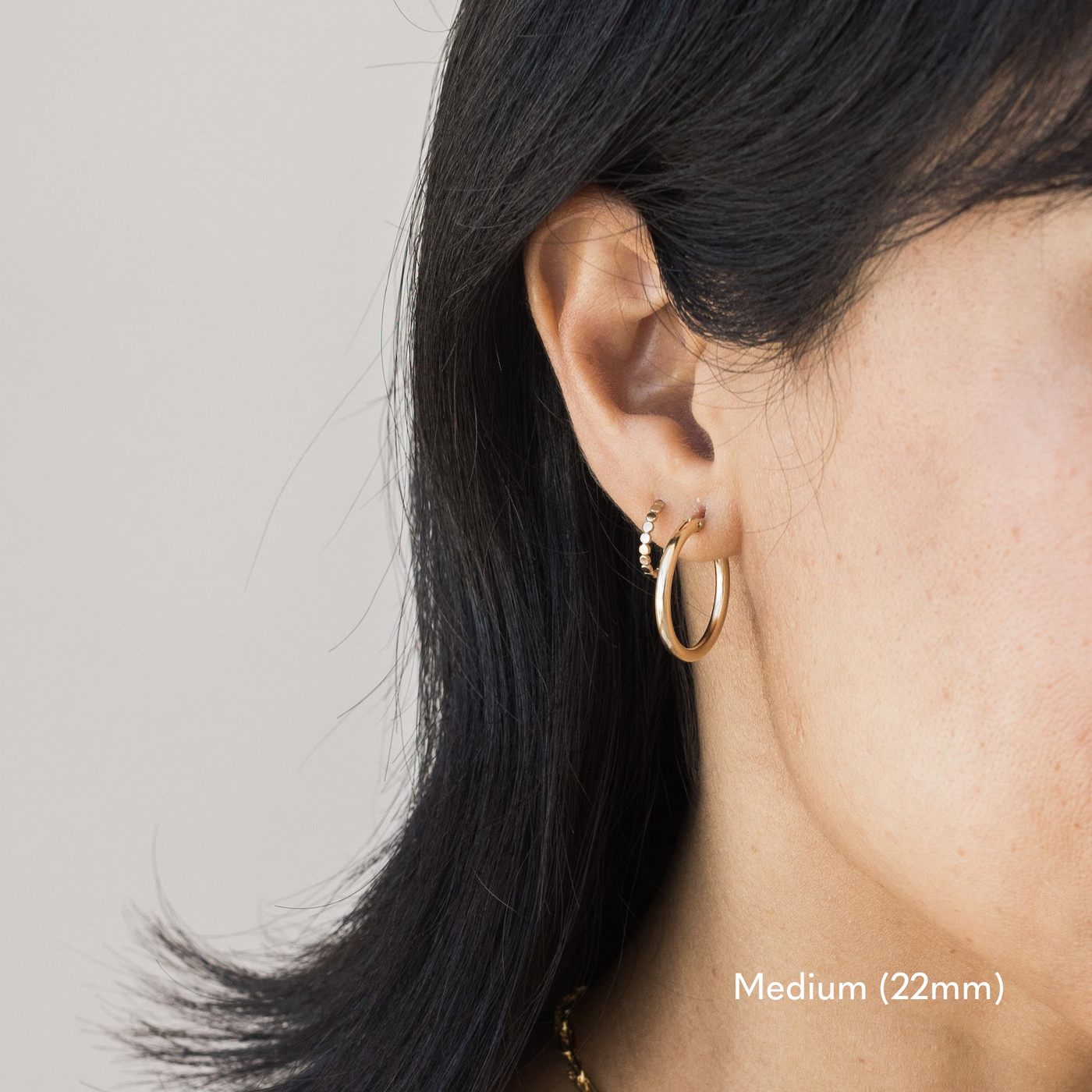 Woman wearing a single medium 22mm gold Everyday Hoop Earring on one ear. The photo is taken from the side, showing her earring, and hair pulled back,.

Medium (22mm) Everyday Hoop Earrings by Simple & Dainty Jewelry