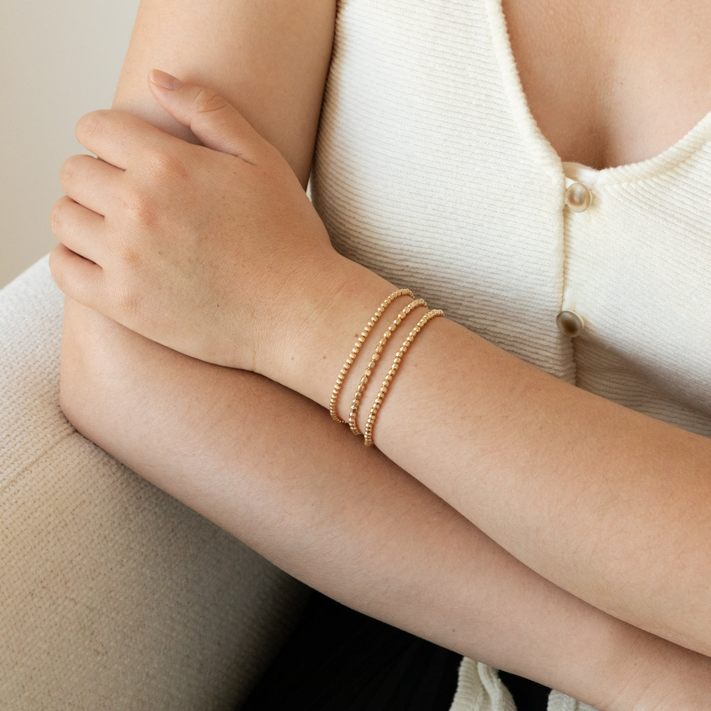 Woman’s forearm with arms crossed, wearing a Ribbed Stretch Bead Bracelet, Faceted Stretch Bead Bracelet, and Hammered Stretch Bead Bracelet.