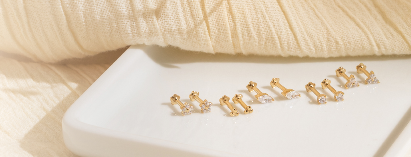 Five pairs of gold vermeil flat back stud earrings displayed on a white ceramic tray.