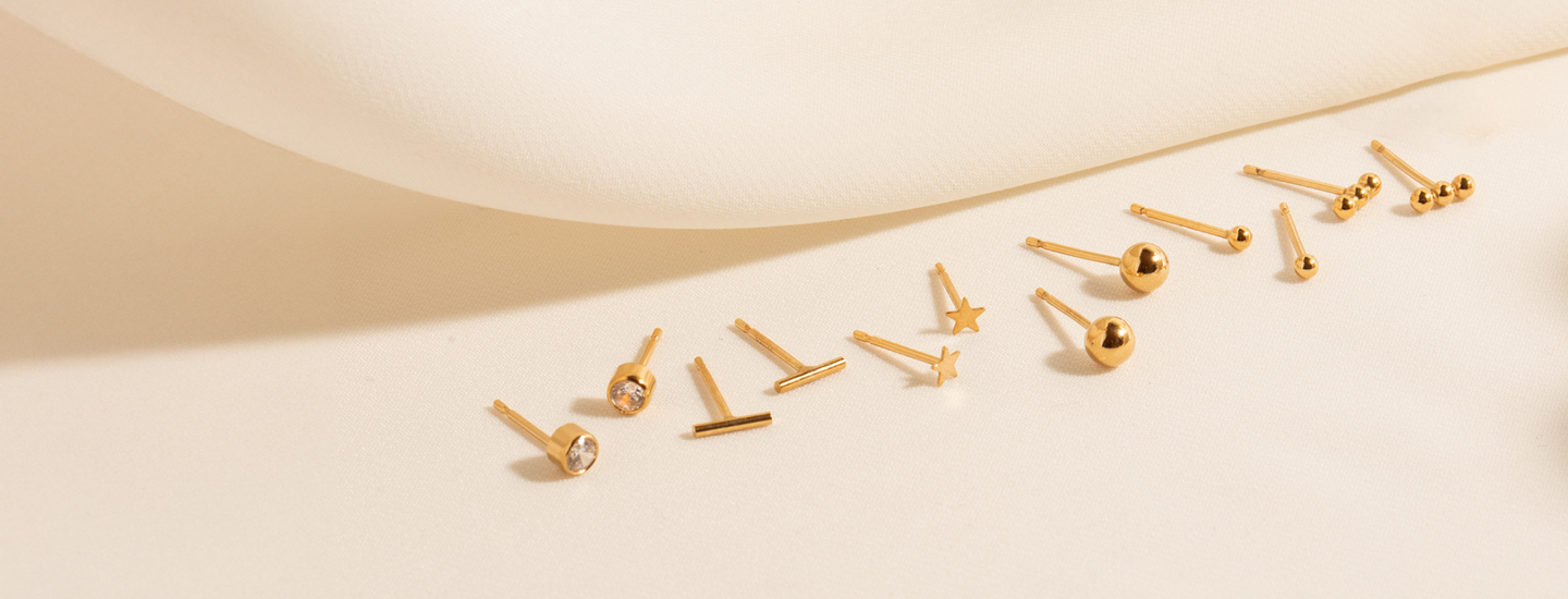 An image of six stud earrings against a cloth background: Dainty CZ Bezel Stud, Tiny Bar Studs, Tiny Star Studs, 4mm Ball Studs, 2mm Ball Studs, and Bead Bar Studs