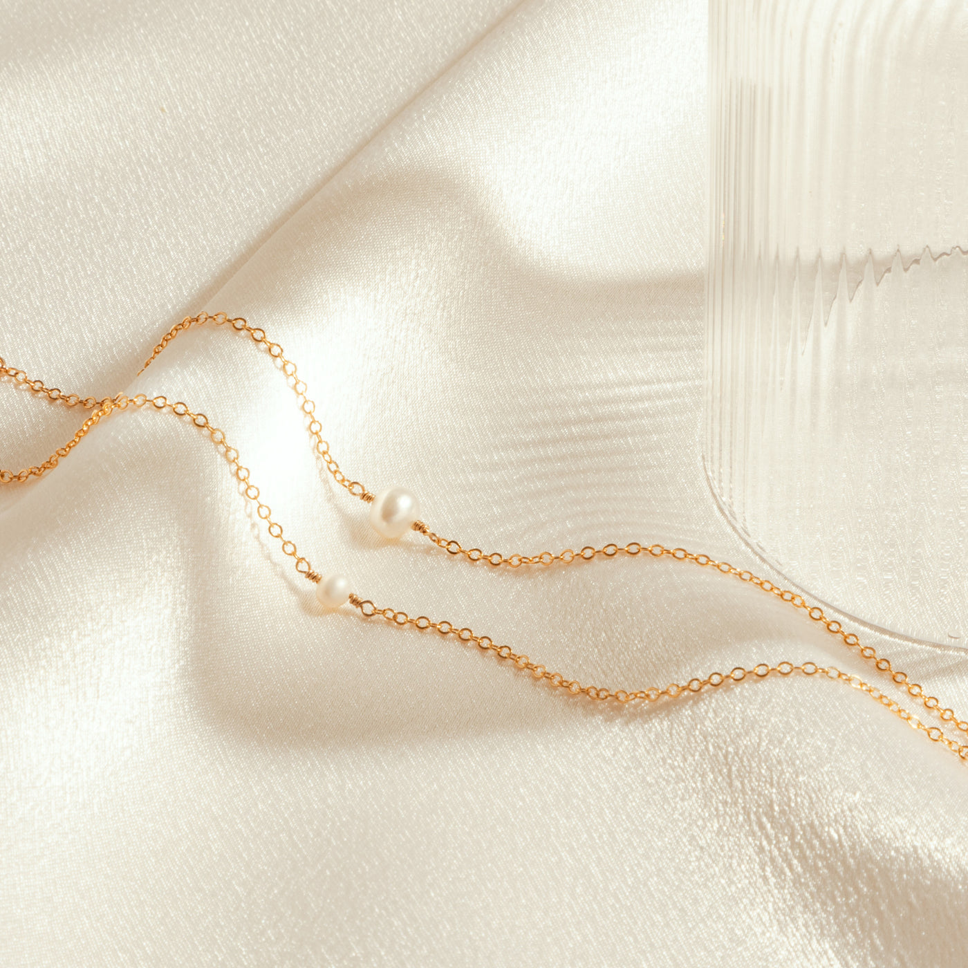 Gold chain necklace with pearls on a soft beige fabric background. Small Large Freshwater Pearl Necklace by Simple & Dainty Jewelry. 