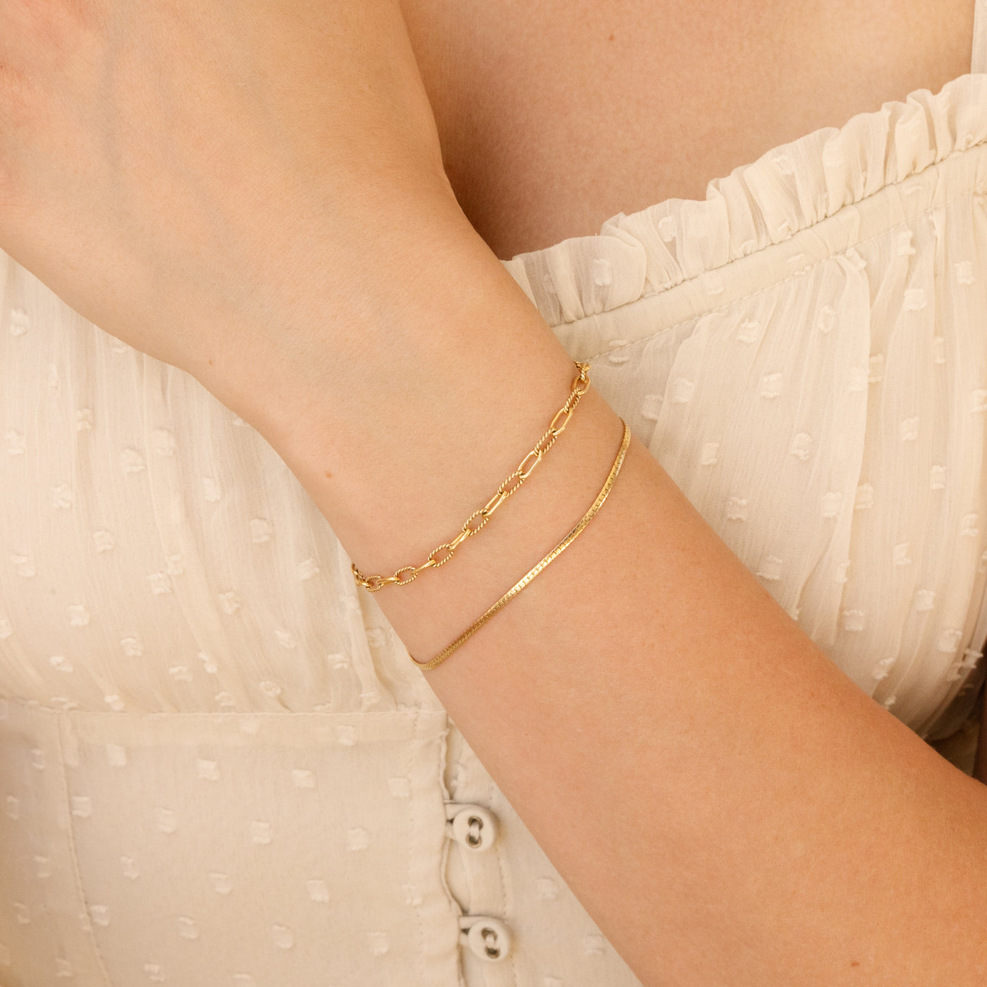 woman's wrist with twisted paperclip chain bracelet and dainty herringbone chain bracelet