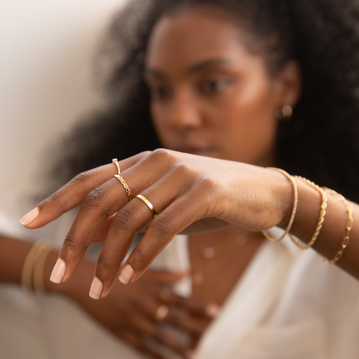Close-up of a hand wearing two gold rings—Twist Ring and Flat Band Ring—and gold bracelets.