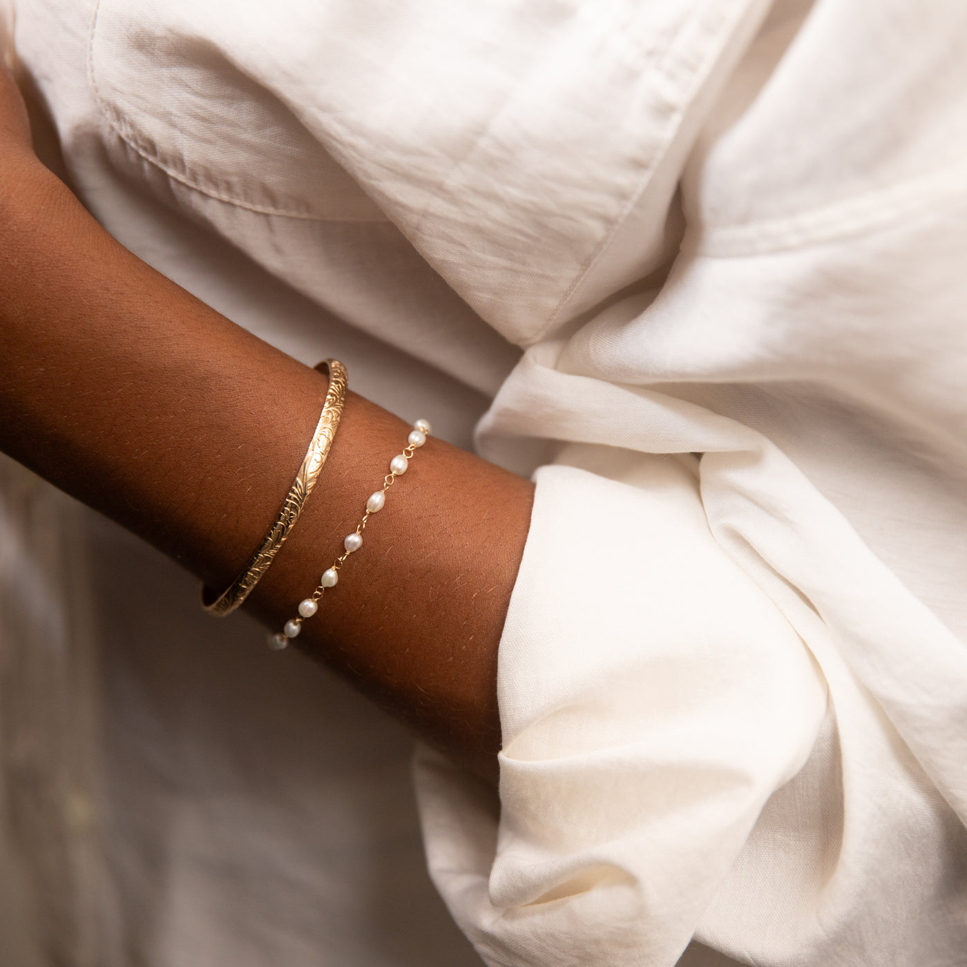 Close-up of a wrist wearing gold and pearl bracelets with a white shirt.