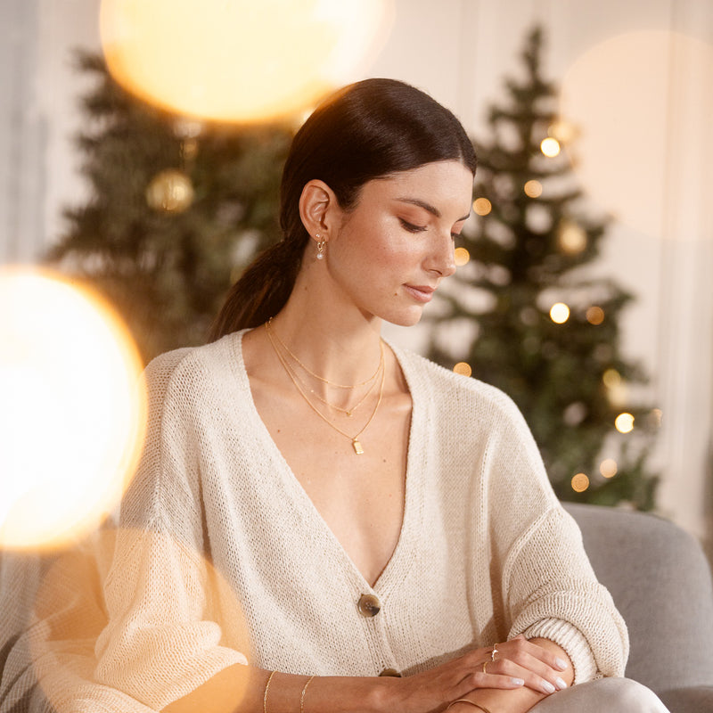 Woman wearing a beige sweater sitting in a cozy room with blurred Christmas trees in the background