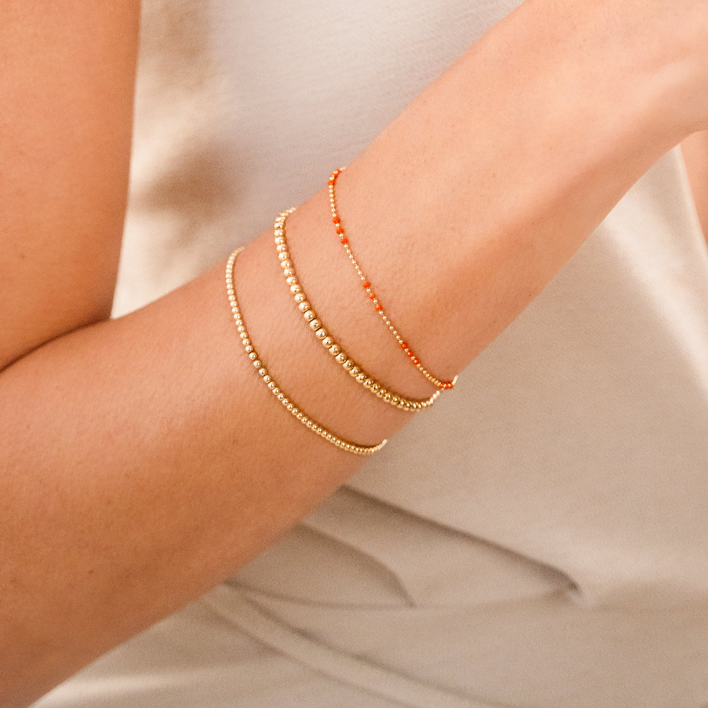 Close-up of a woman's wrist wearing the Red Enamel Ball Chain Bracelet and two Stretch Bead Bracelets.