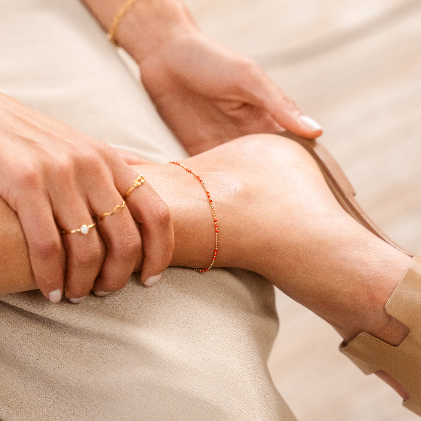 Close-up of a woman's foot wearing the Red Enamel Ball Chain Anklet. She’s also wearing three rings and sandals.