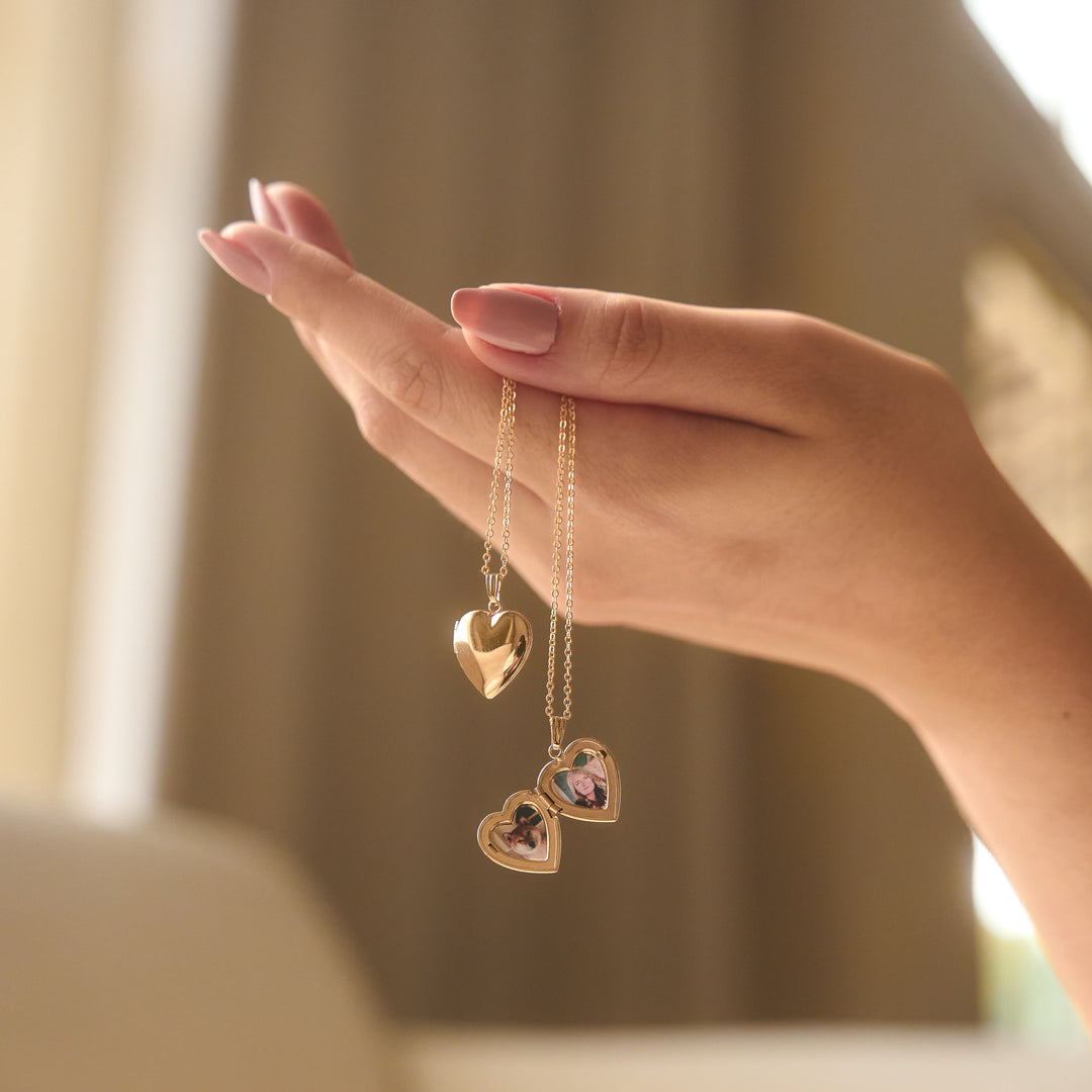 A gold locket pendant on a chain, open to reveal two interior photos, against a white background.