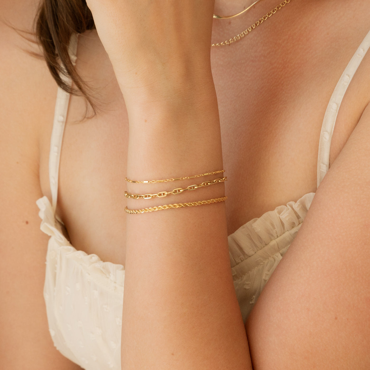 Close up of woman's arm against chest, she's wearing 3 gold filled bracelets including sparkly soda and french rope chain bracelets