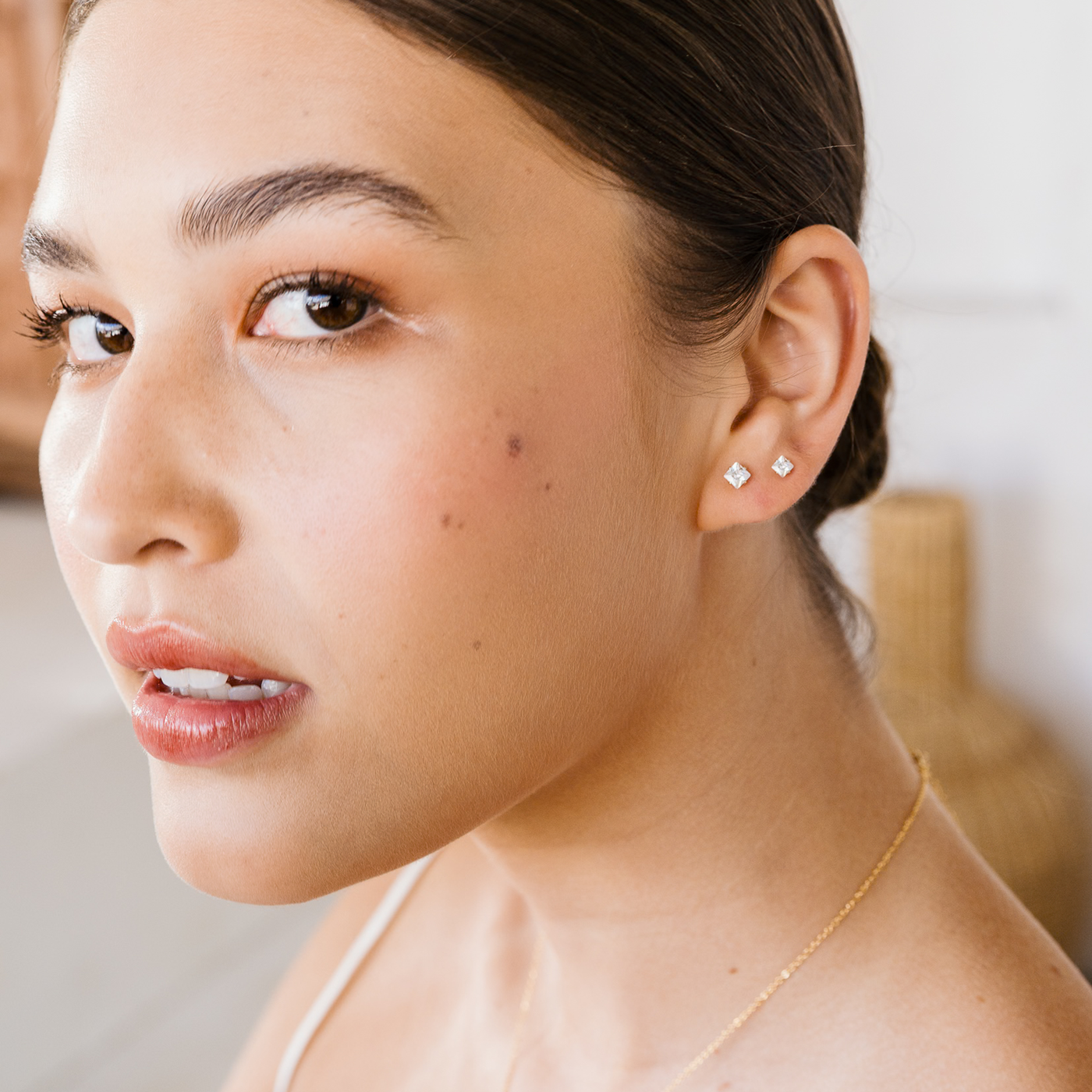 3mm 4mm Dainty Square CZ Stud Earrings. Close-up of a woman wearing diamond stud earrings with a blurred background