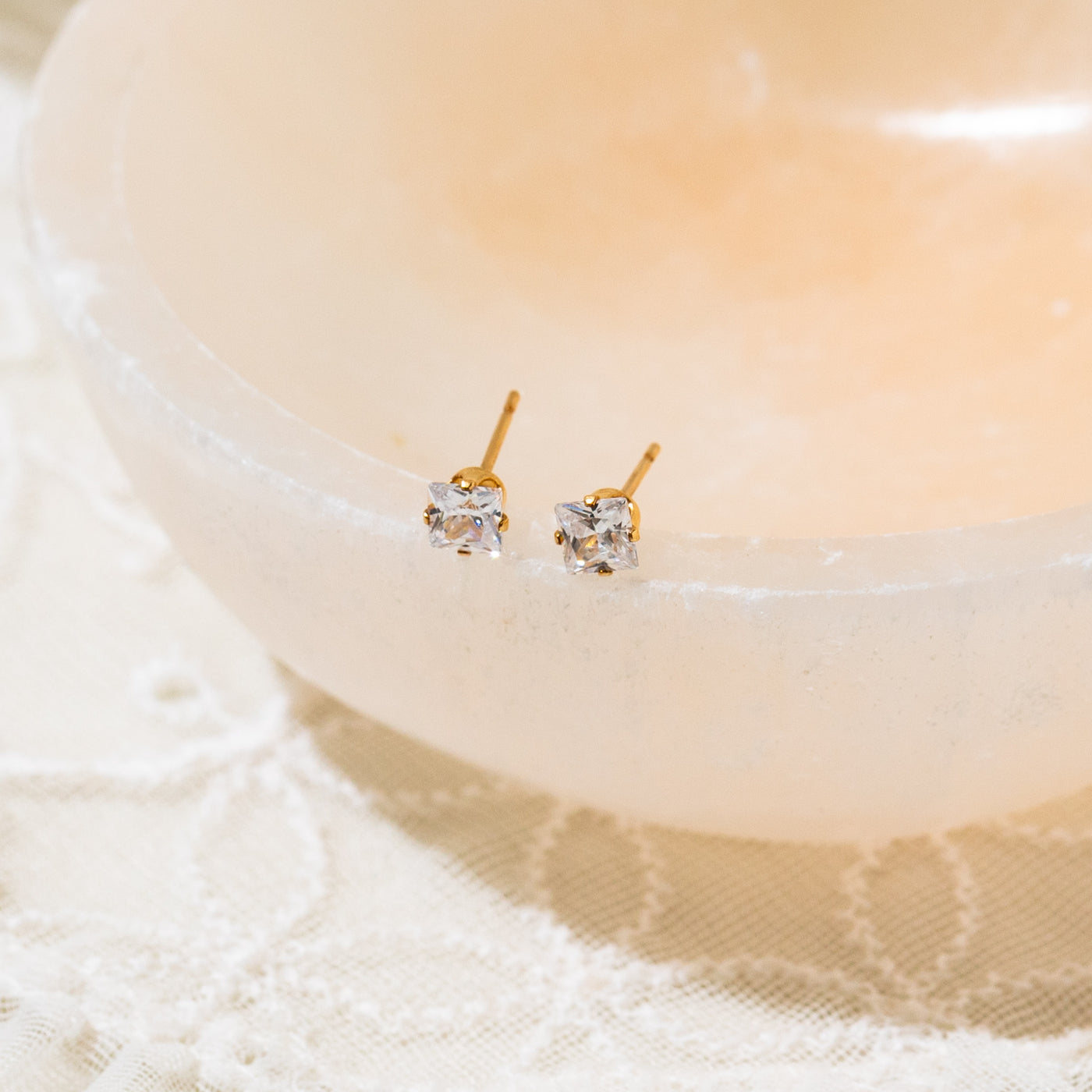 3mm 4mm Dainty Square CZ Stud Earrings. Gold stud earrings on a white dish with a soft focus background