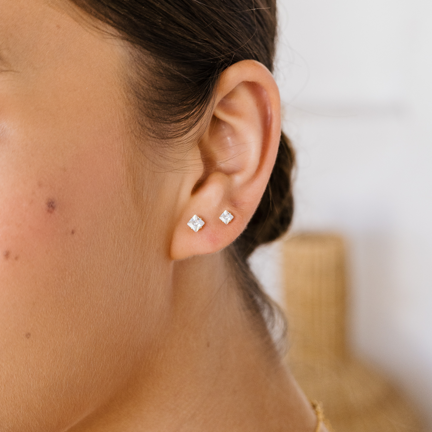 3mm 4mm Dainty Square CZ Stud Earrings. Close-up of an ear wearing two diamond stud earrings with a blurred background.