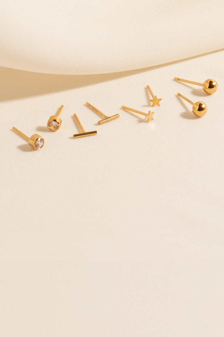 An image of six stud earrings against a cloth background: Dainty CZ Bezel Stud, Tiny Bar Studs, Tiny Star Studs, 4mm Ball Studs, 2mm Ball Studs, and Bead Bar Studs