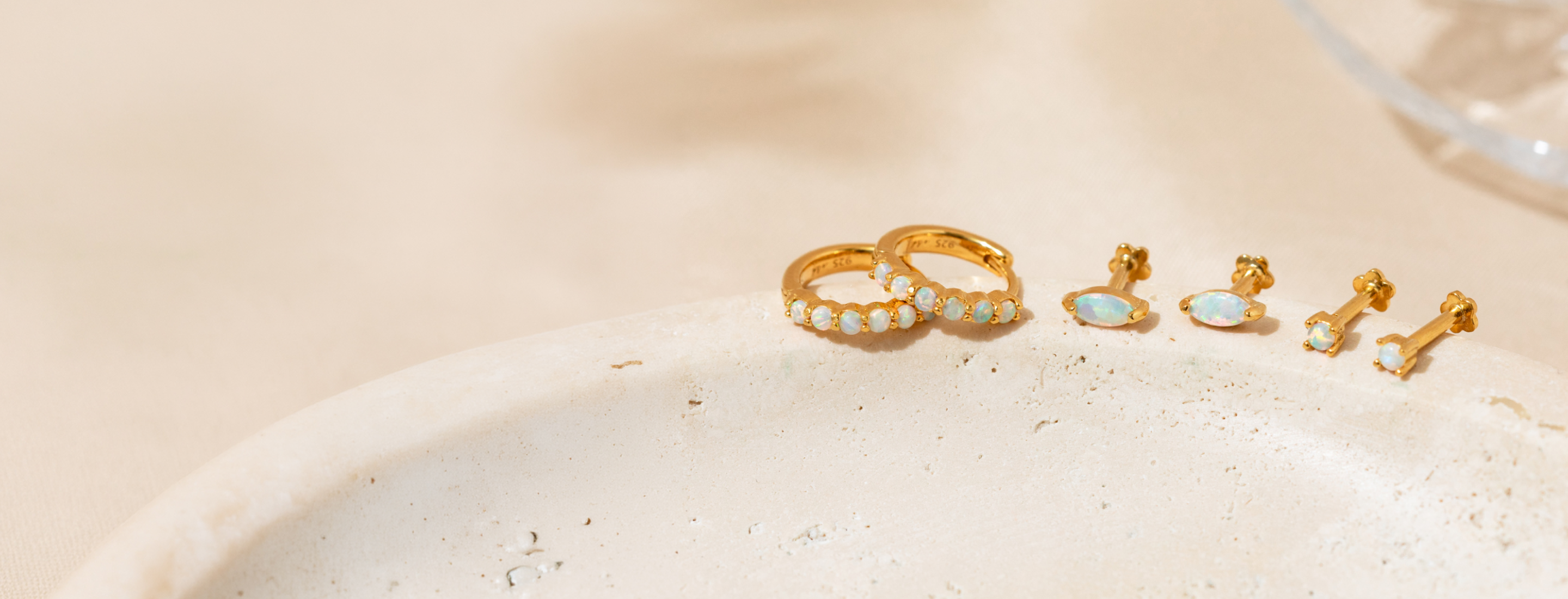 Opal huggie hoop earrings, marquise opal flat back studs, and dainty opal earrings displayed on a natural stone surface.