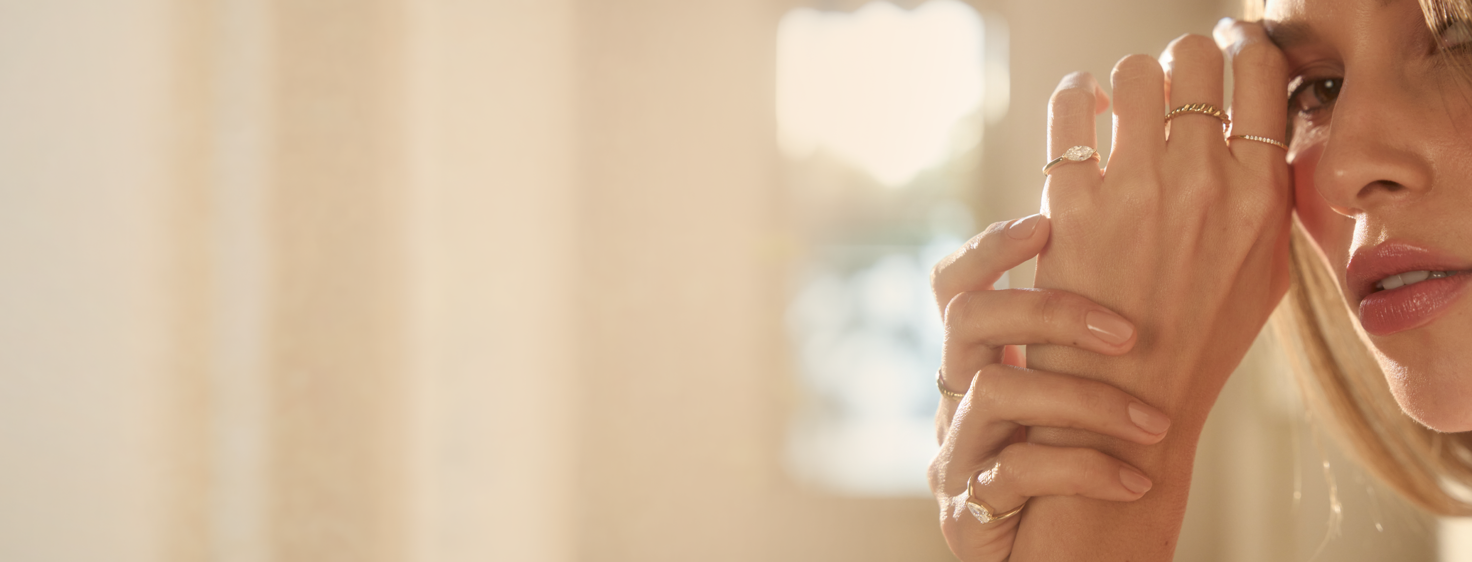 Woman waering gold rings with her hand next to her face.
