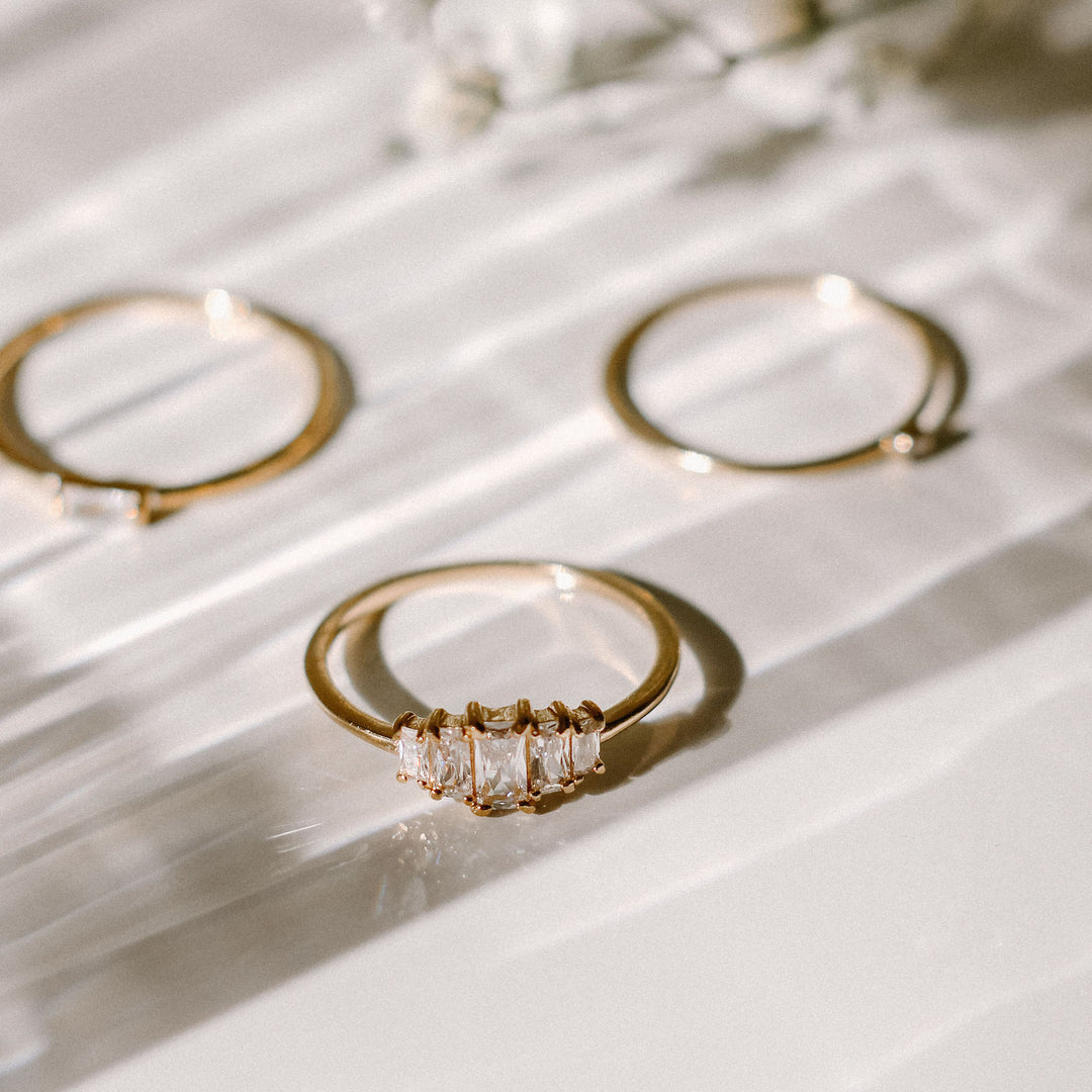 Three gold rings with cubic zirconia stones on a white surface.