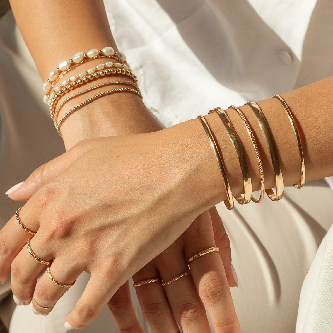 A woman's hands adorned with gold bangles, pearl bracelets, and delicate rings, resting on her lap.