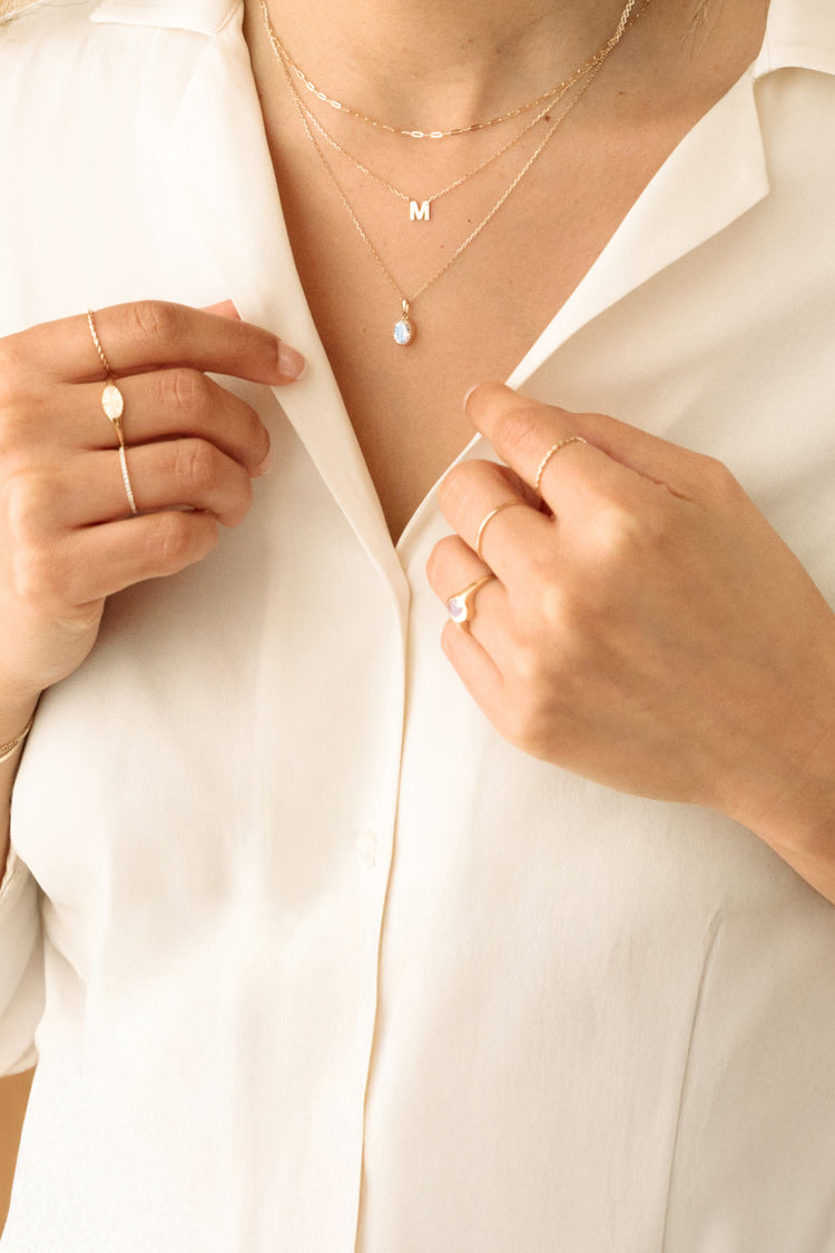 Women in white shirt wearing hoop earrings and 3 necklaces including an initial necklace, a moonstone necklace, and a chain necklace.