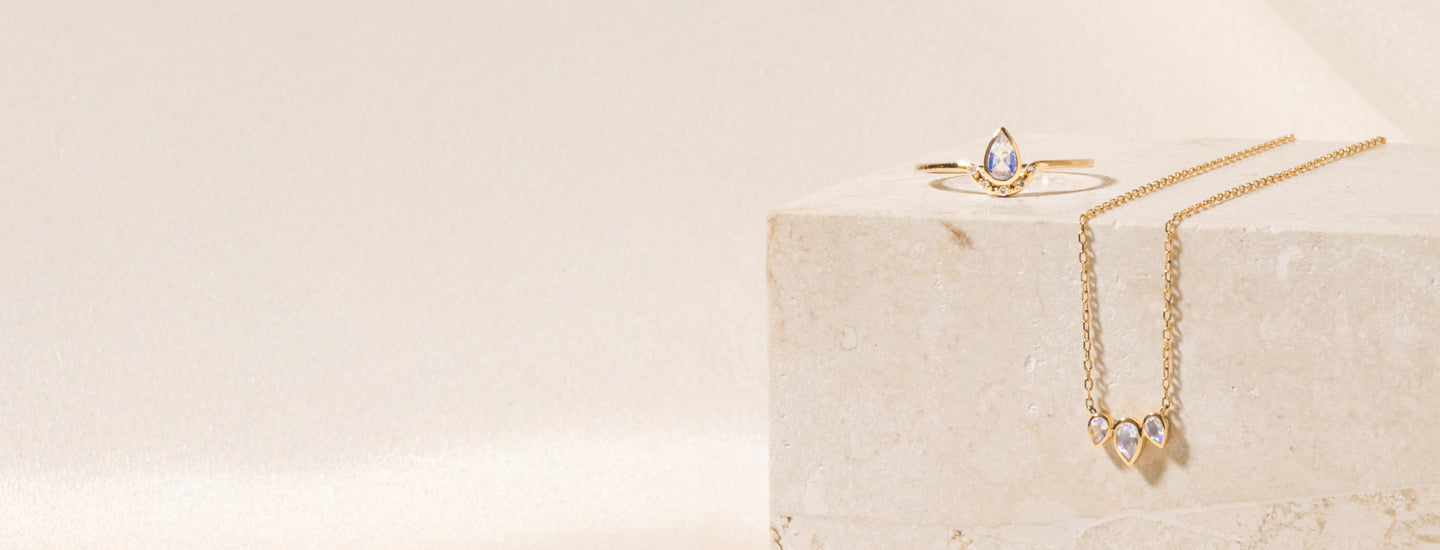 Moontone teardrop ring and triple teardrop moonstone necklace on a travertine block