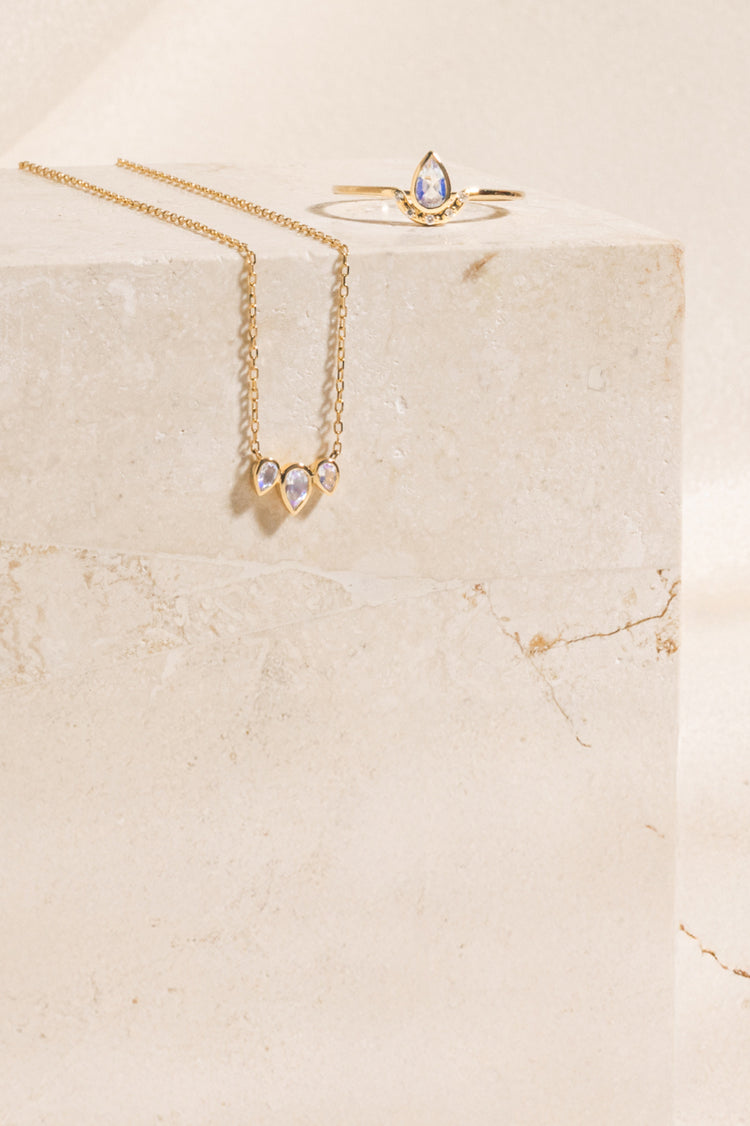 Moontone teardrop ring and triple teardrop moonstone necklace on a travertine block