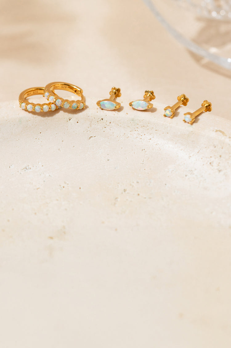 Opal huggie hoop earrings, marquise opal flat back studs, and dainty opal earrings displayed on a natural stone surface.