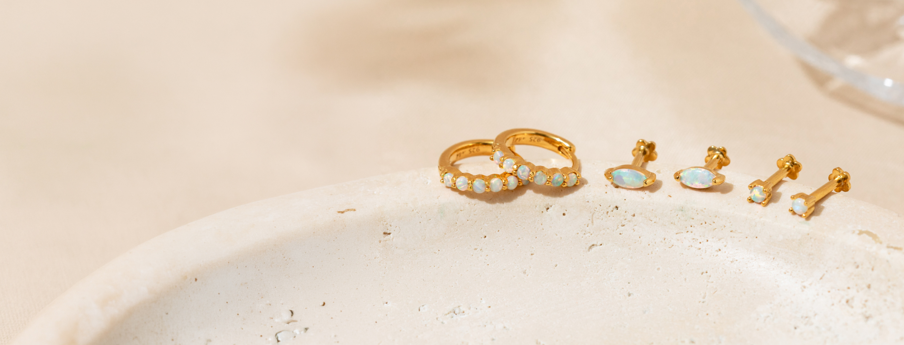 Opal gold filled hoop earrings and stud earrings on a textured beige surface
