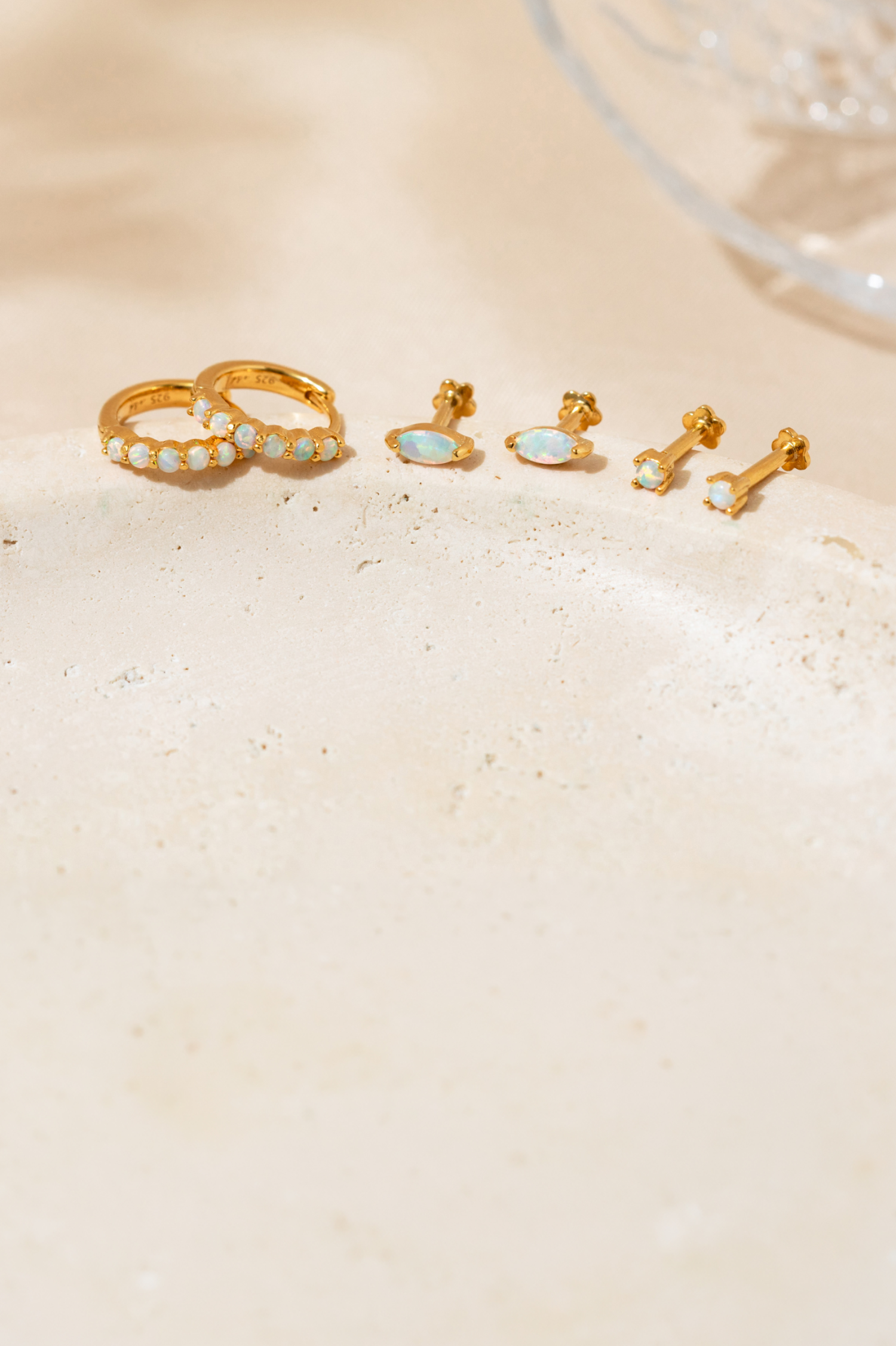 Opal gold filled hoop earrings and stud earrings on a textured beige surface