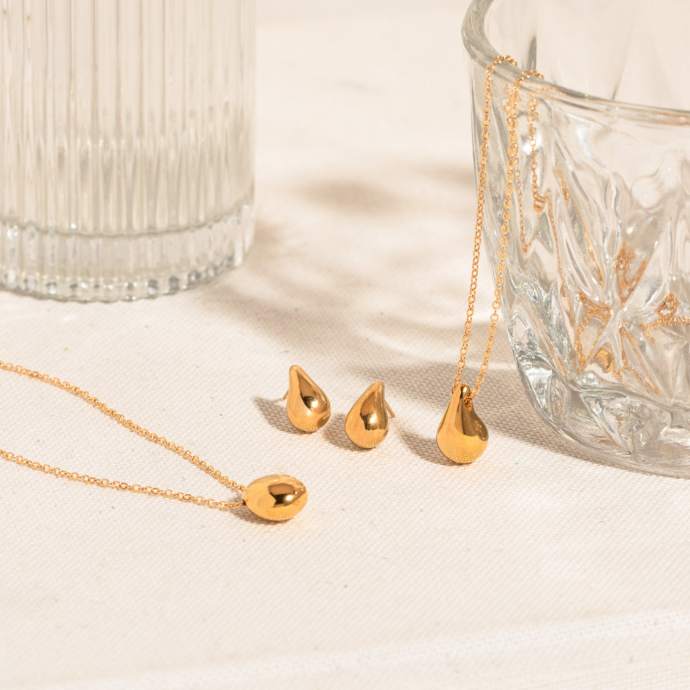 Pebble necklace, teardrop earrings, and teardrop necklace lying on a white textured surface with two crystal bowls.
