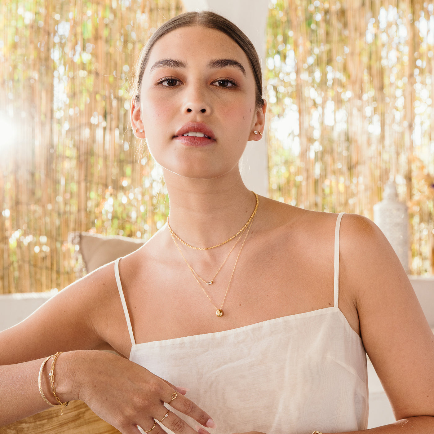 Woman in white tank top looking wearing 3 necklaces, including french rope, dainty baguette, and pebble necklace.
