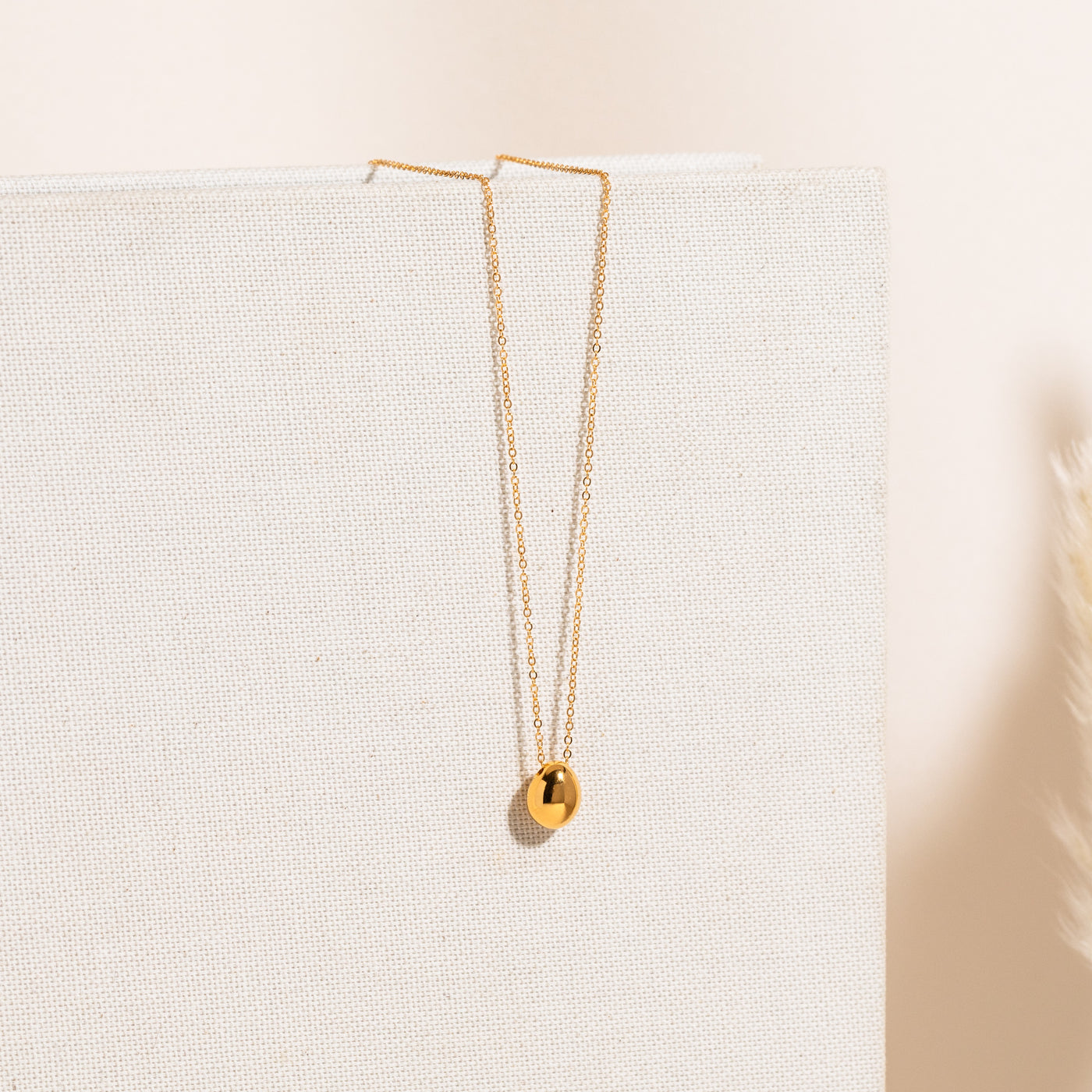 Delicate pebble necklace displayed vertically on a textured white fabric backdrop