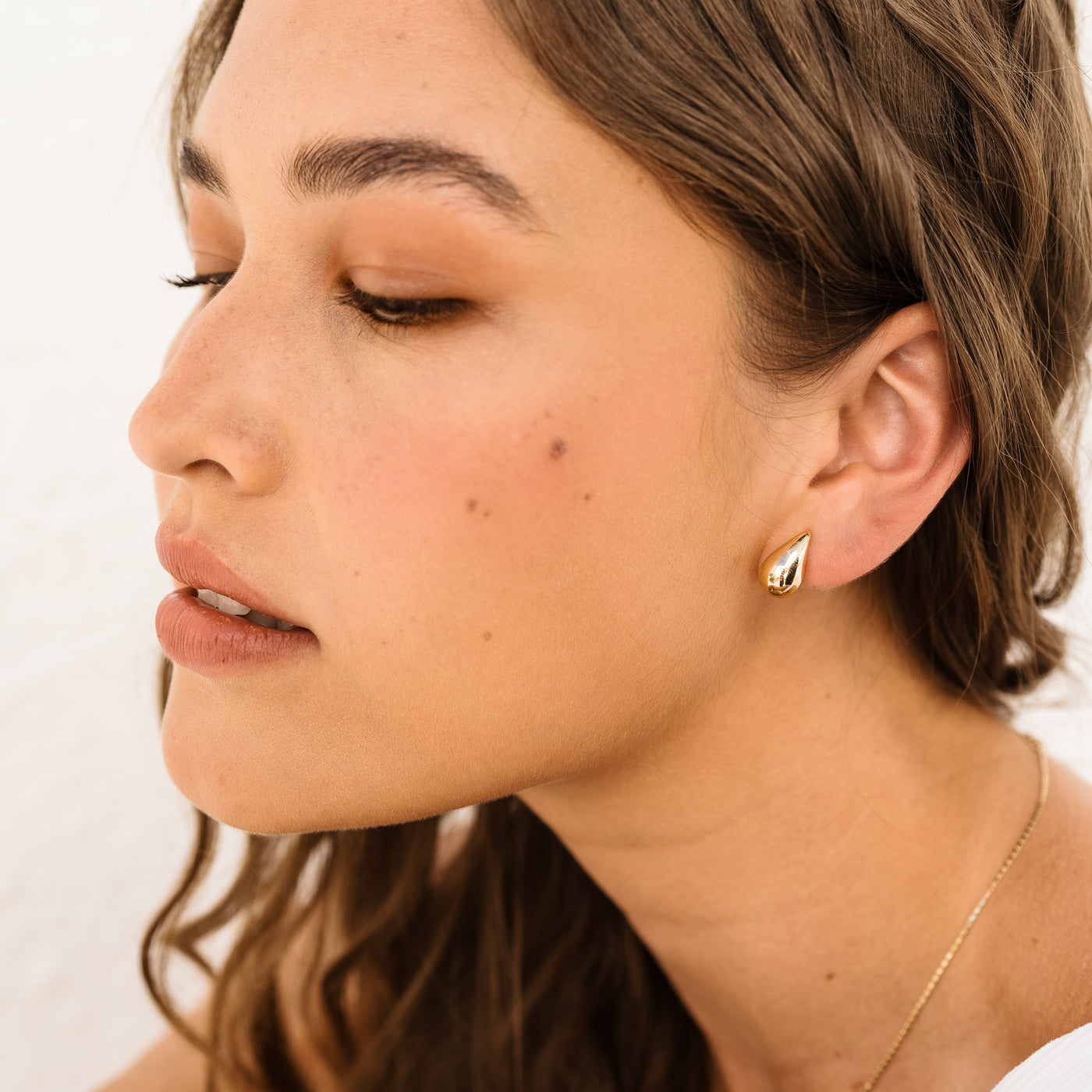 Small Large Teardrop Stud Earrings. Woman's face looking to the side. She's wearing 14k solid gold stud earrings