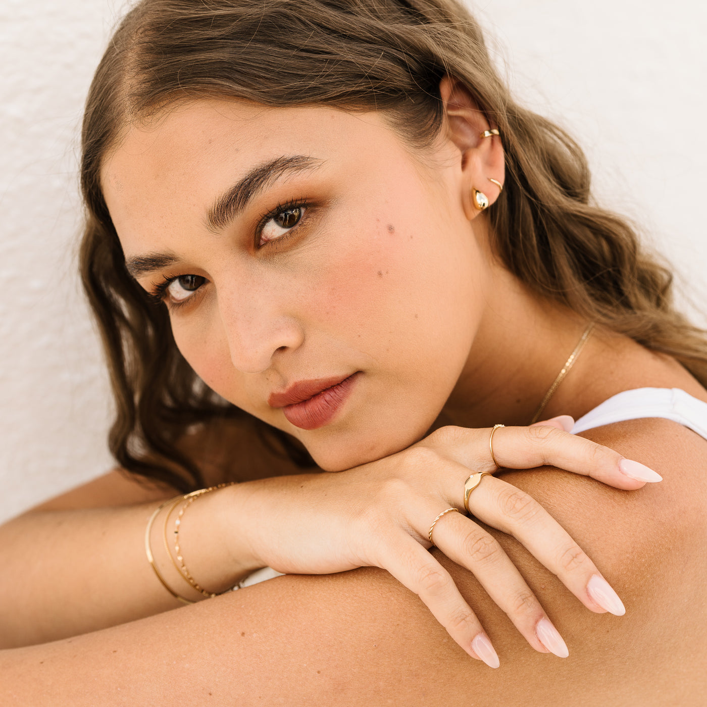Small Large Teardrop Stud Earrings. Woman resting her chin on her hand, wearing a twist ring, diamond signet ring, and dainty ring. She also has on teardrop stud earrings, a hoop, and an ear cuff.