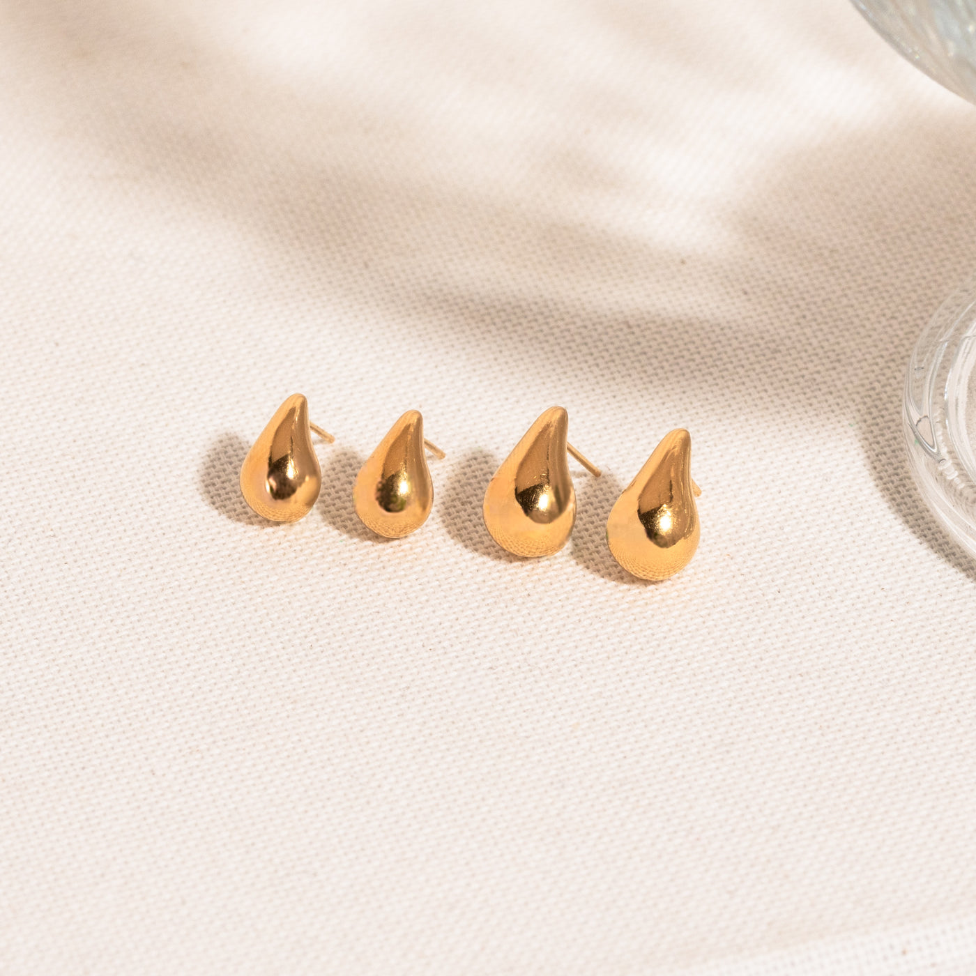 Small Large Teardrop Stud Earrings. Dainty teardrop stud earrings and teardrop stud earrings lying on white textured surface