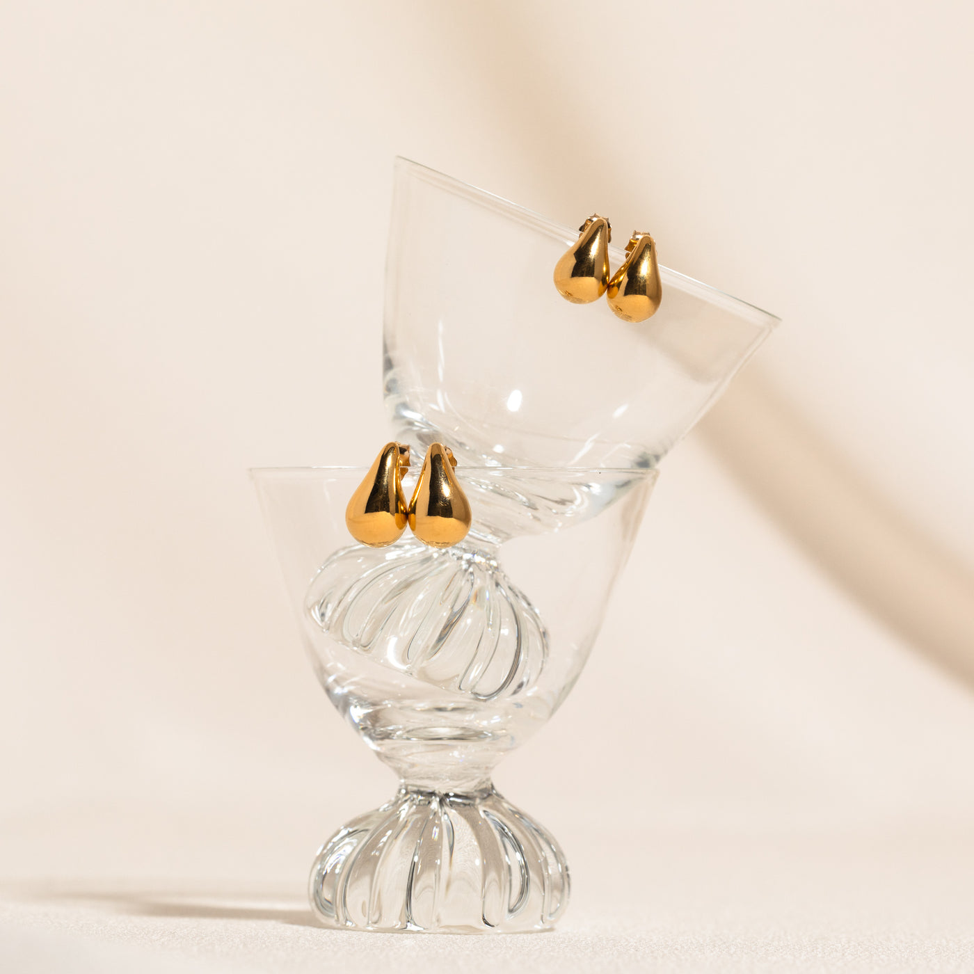 Small Large Teardrop Stud Earrings. 14k solid gold stud earrings, one smaller pair and one larger pair, resting on the edge of stacked glass cups in balance.