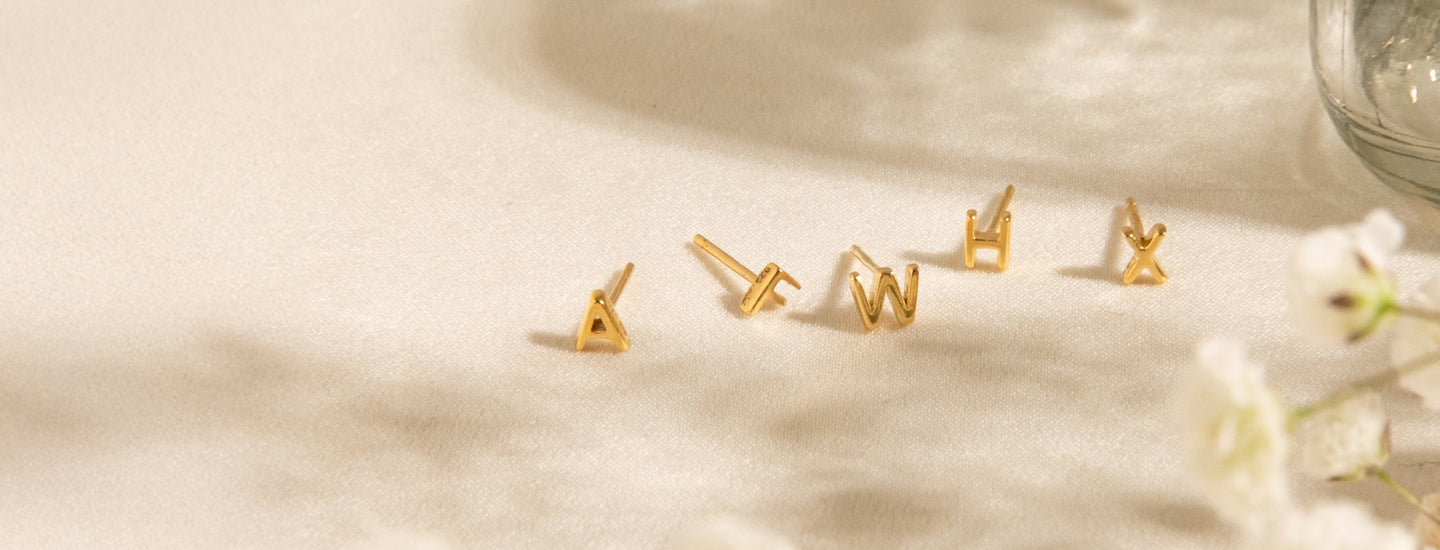 Tiny Initial Stud Earrings on light backgorung with flower