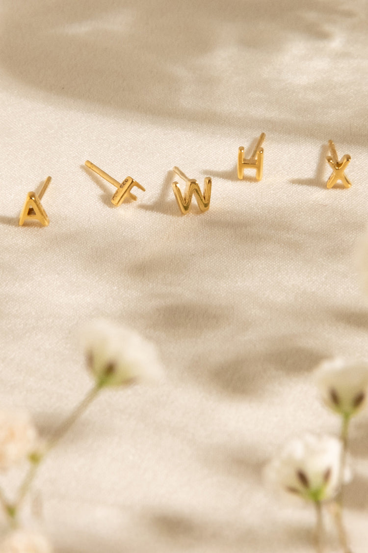 Tiny Initial Stud Earrings on light backgorung with flower
