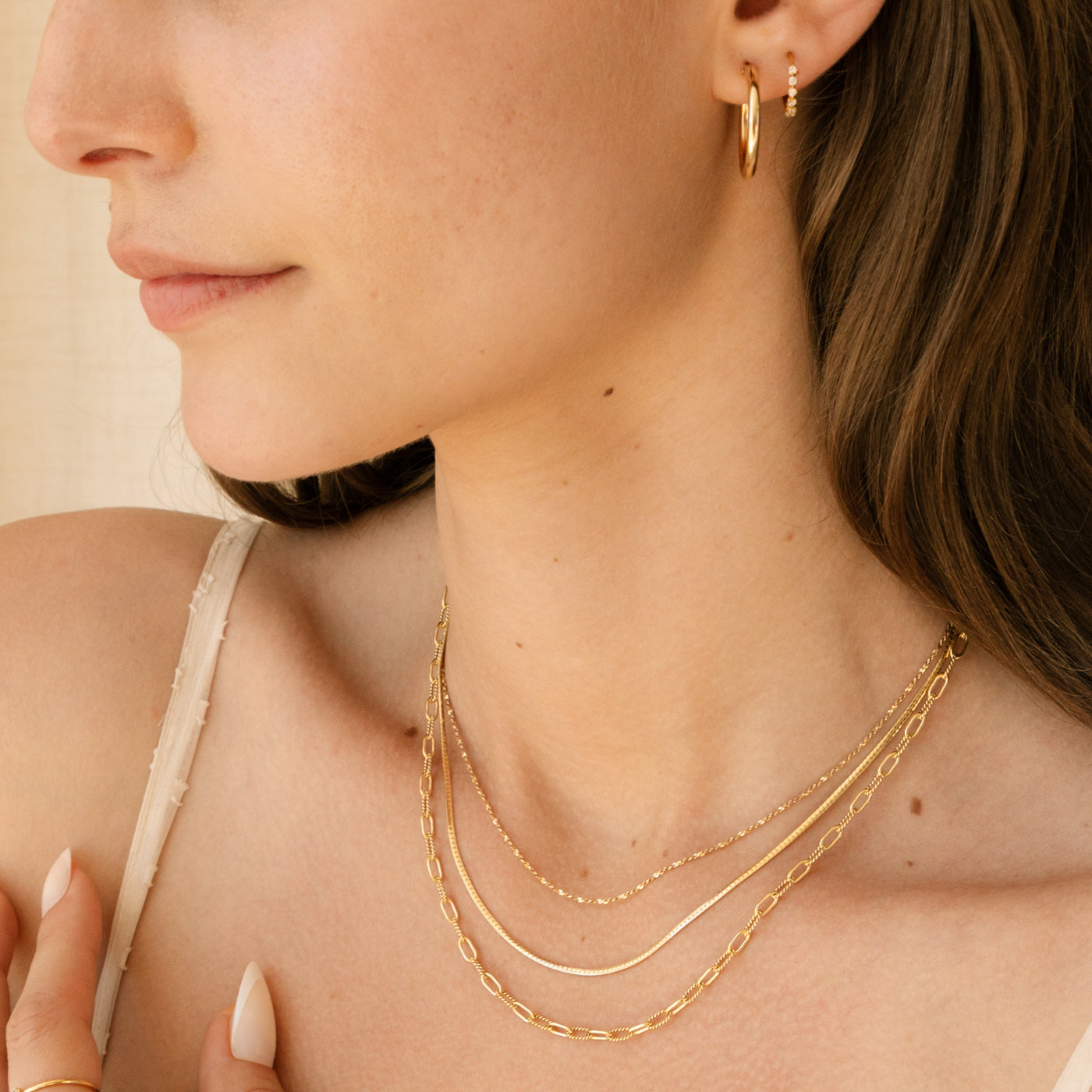 Woman's neck close-up. She's wearing 3 chain necklaces including herringbone, paperclip, and sparkly chains