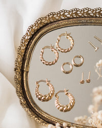 Two pairs of chunky hoops, a pair of huggies, and two pairs of stud earrings displayed on a vintage lace-edged mirror.