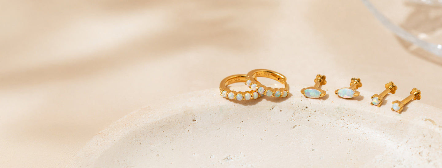 Opal huggie hoop earrings, marquise opal flat back studs, and dainty opal earrings displayed on a natural stone surface.