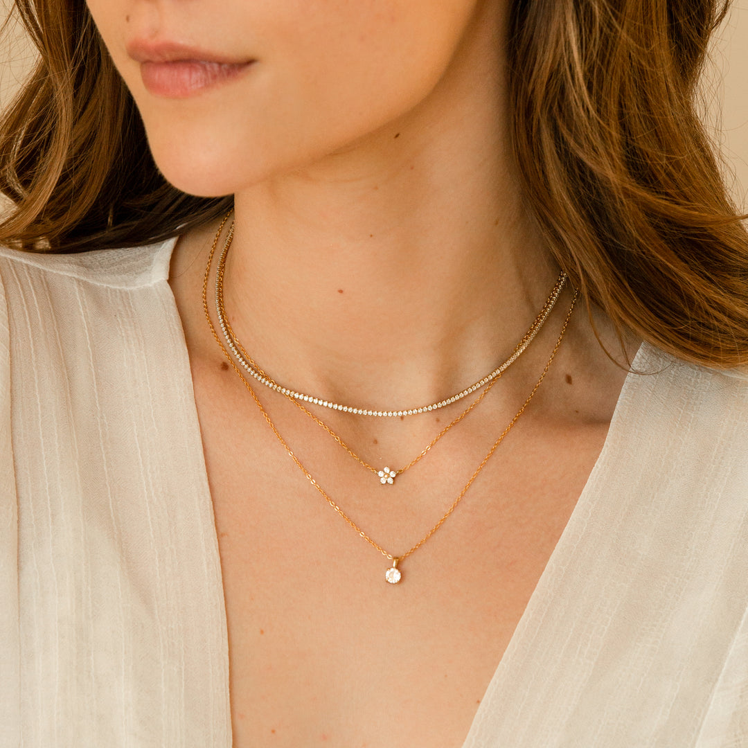 Woman wearing three gold necklaces: Dainty CZ Tennis Necklace, Dainty Flower CZ Necklace, and Hanging Solitaire Necklace.
