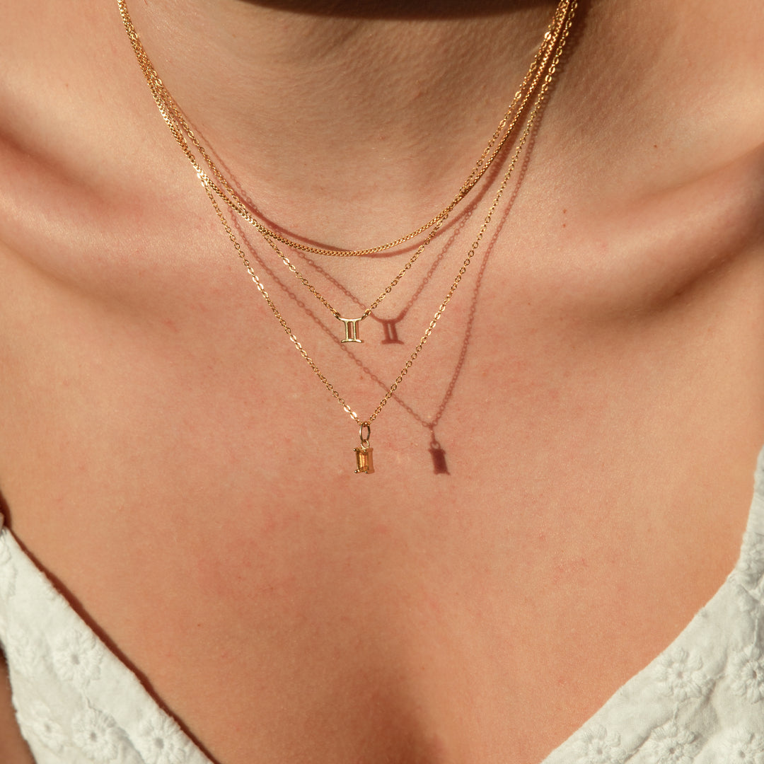 A woman wearing a gold chain necklace, layered with two gold charm necklaces at different lengths.